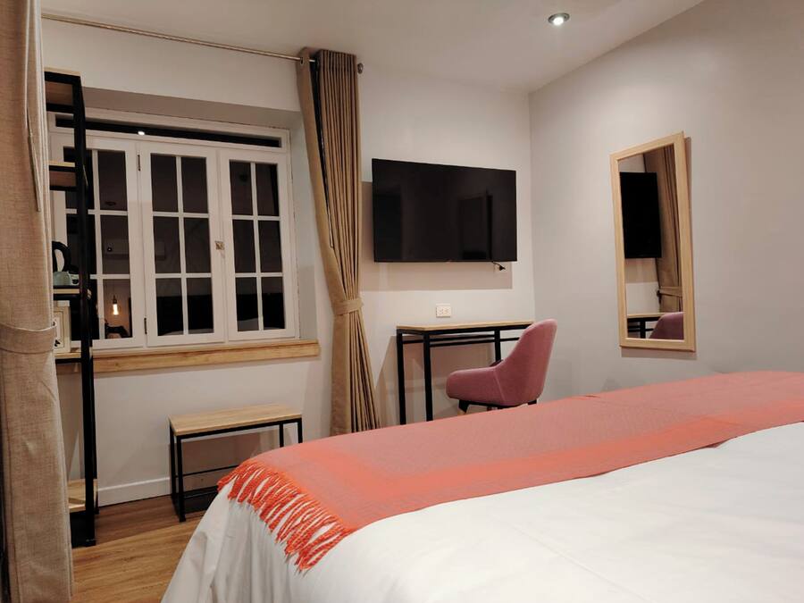 Habitación de hotel con cama, escritorio, silla, televisor, ventana con cortinas y espejo.