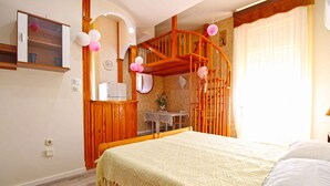 Un dormitorio con una cama de madera, una mesita, una silla, una escalera de madera y una ventana con cortinas.