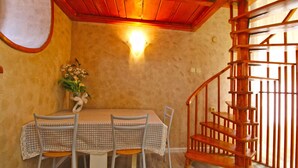 Un área de comedor con una mesa y sillas, una escalera de madera y una lámpara fijada a la pared.