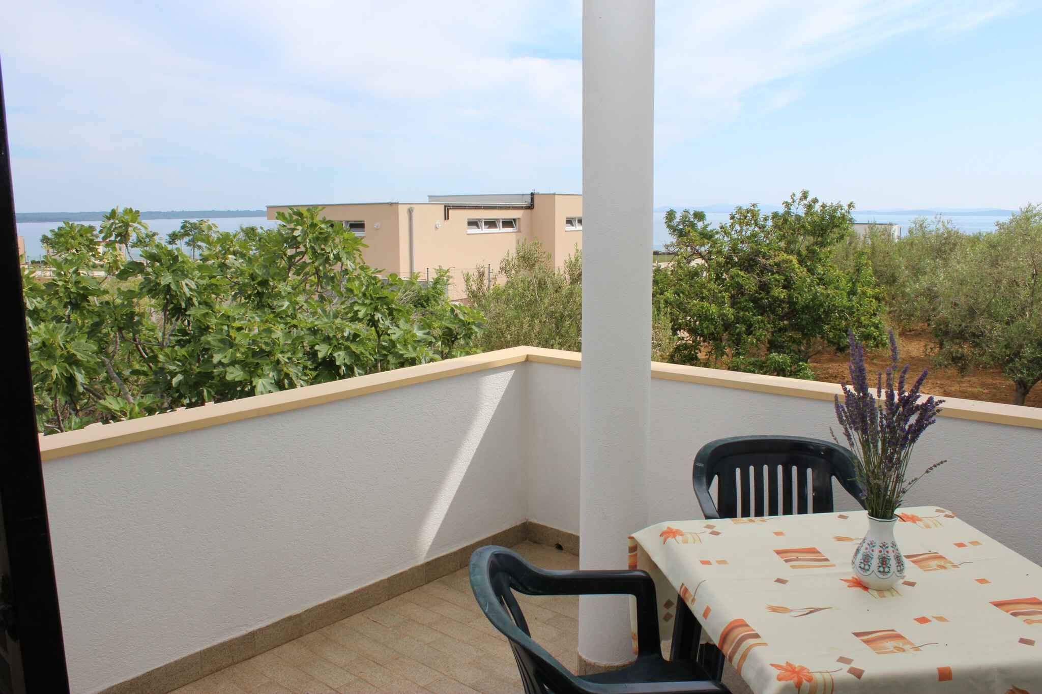 Uma varanda com mesa e cadeiras, um vaso com flores e vista para edifícios e áreas verdes.