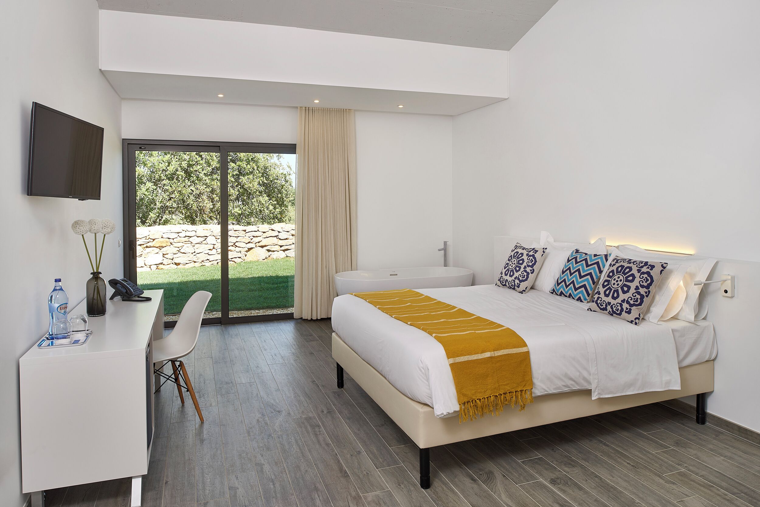 A modern bedroom with a bed, desk, chair, and a TV mounted on the wall.