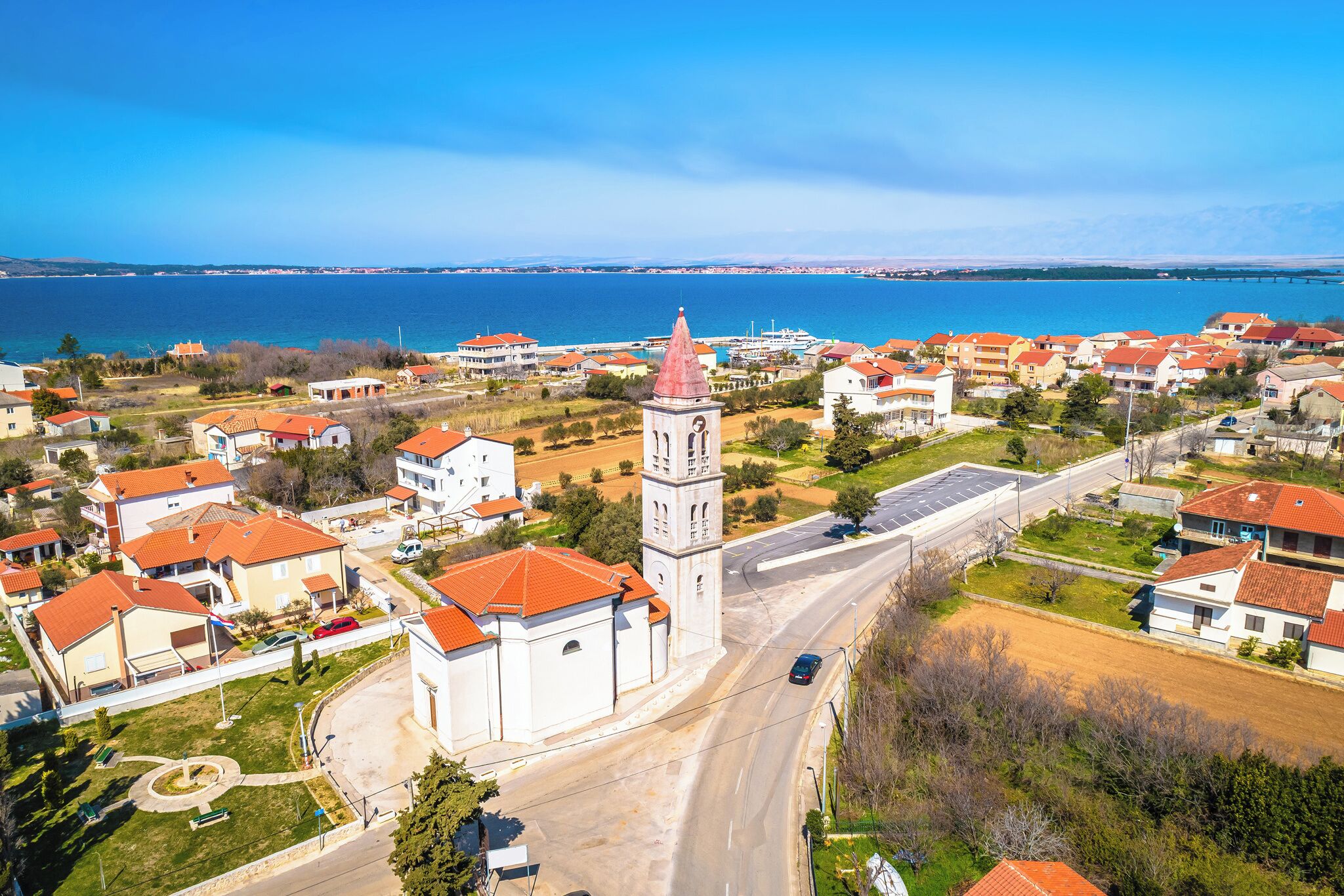 A coastal town with a prominent church tower, residential buildings, and a clear view of the sea.
