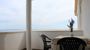 Een balkon met een tafel en stoelen, een vaas met planten en uitzicht op de zee en verre bergen.