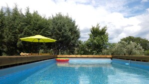 Une piscine à l’eau d’un bleu cristallin, entourée d’arbres et bordée d’une terrasse en bois.