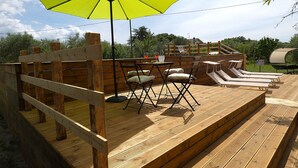 A wooden deck with outdoor seating, including chairs and a table, under a large umbrella. - Scappo in Umbria, Felicità 14a (Giove)