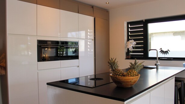 A modern kitchen with white cabinets, a black countertop, and a wooden bowl with pineapples. - Luxury Villa Incl Pool With Seaview Near Beaches (Grote Berg)