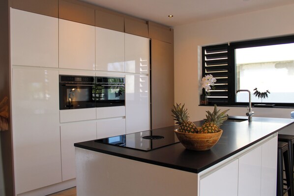 A modern kitchen with white cabinets, a black countertop, and a wooden bowl with pineapples. - Luxury Villa Incl Pool With Seaview Near Beaches (Grote Berg)