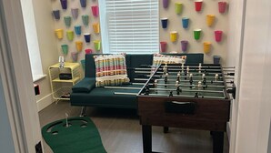 A room with a foosball table, a sofa, a window with blinds, and a wall decorated with colorful plastic cups. - Cozy Stay in NYC!! (New York)