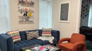 A living room with a blue sofa, an orange armchair, a glass coffee table, and a wall-mounted air conditioner. - Cozy Stay in NYC!! (New York)