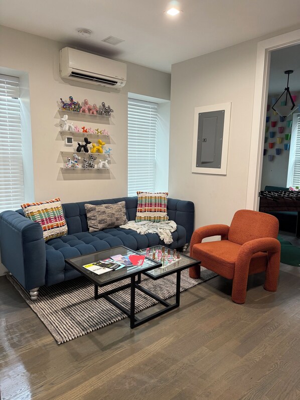 Ein Wohnzimmer mit einem blauen Sofa, einem orangefarbenen Sessel, einem Glastisch und einer Wand-Klimaanlage.