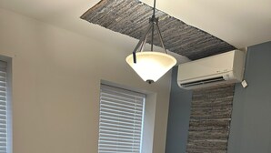 A bedroom with a bed, a bench, a bedside table, and an air conditioning unit. - Cozy Stay in NYC!! (New York)