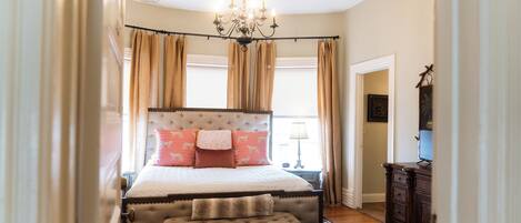 A bedroom with a large bed, a chandelier, a nightstand, and a dresser.