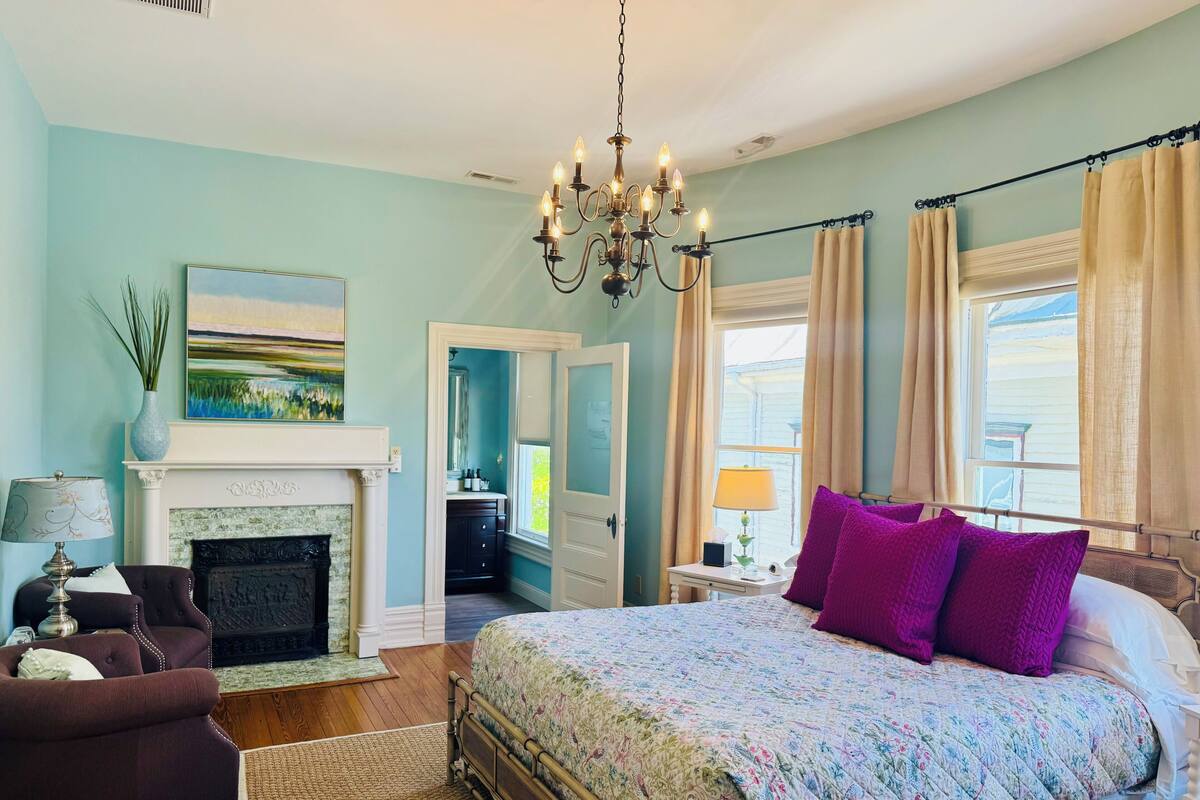 Quarto com cama, lareira, candelabro e vista para o exterior.