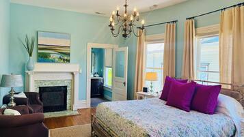 A bedroom with a bed, a fireplace, a chandelier, and a view of the outdoors.