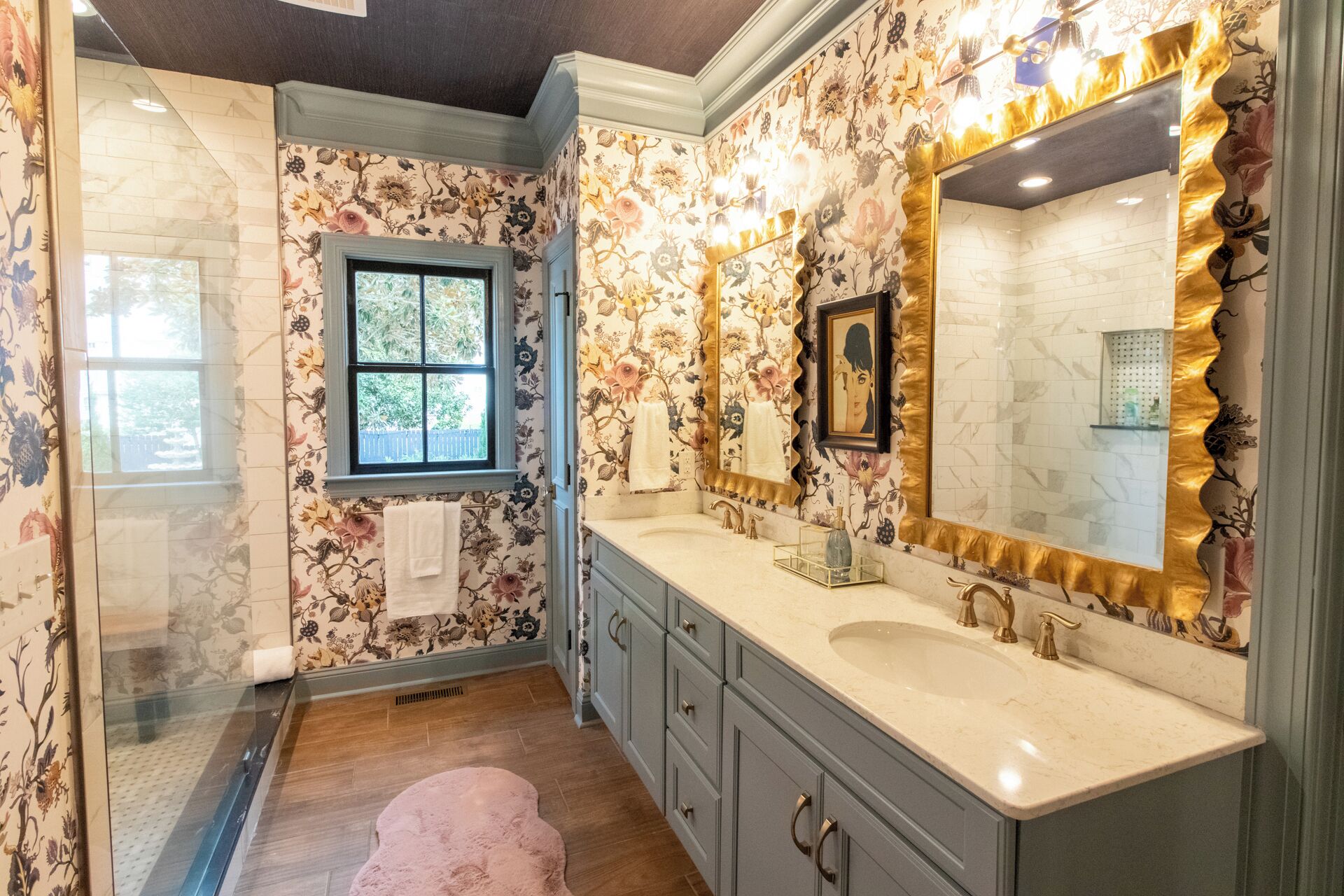 A bathroom with floral wallpaper, a large mirror, a double sink, and a window.