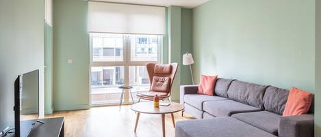 A modern living room with a grey sofa, a brown leather chair, a small round table, and a TV on a wooden stand.