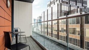 A balcony with a table and chairs, a clock on the wall, and a view of a cityscape with modern buildings. - Native Victoria (London)