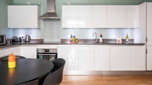 A modern kitchen with white cabinets, a stainless steel range hood, and a wooden dining table with chairs. - Native Victoria (London)
