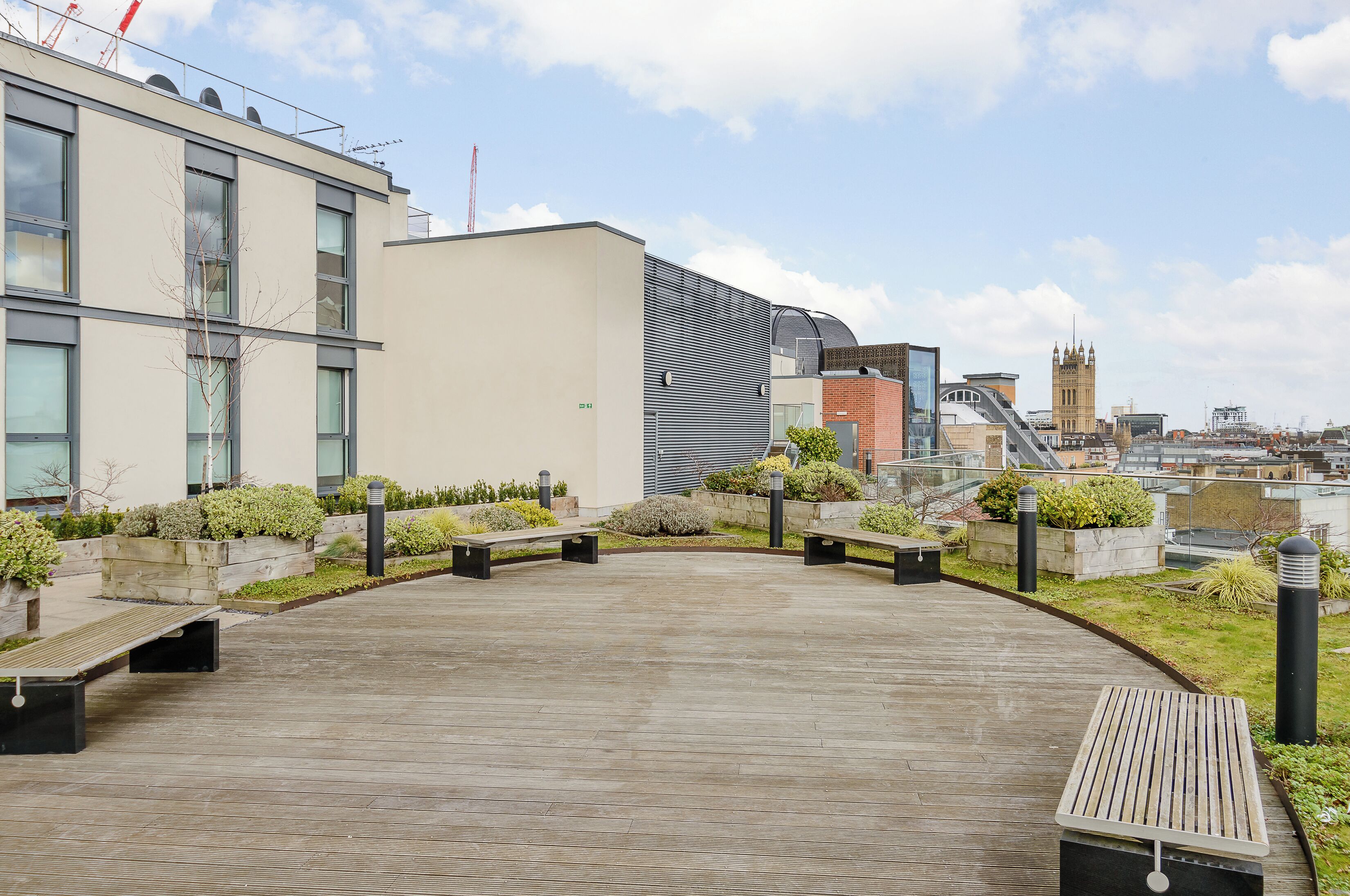 A rooftop terrace with wooden flooring, benches, and planters.