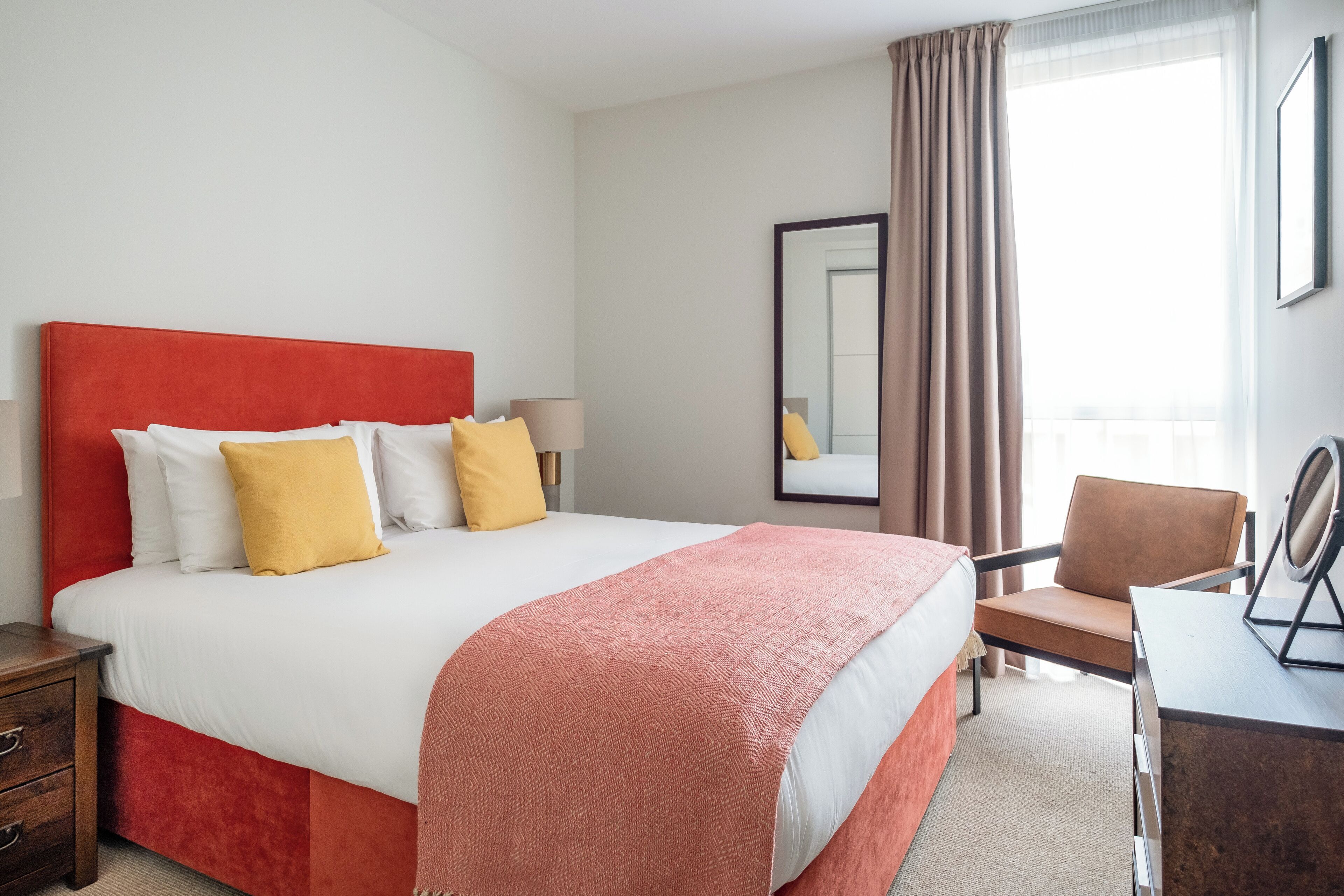 A hotel room with a large bed, a desk, a chair, a mirror, and a window with curtains.