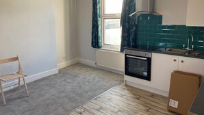 Une cuisine avec une fenêtre, un radiateur, une cuisinière et un plancher en bois.