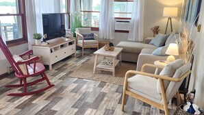 A living room with a TV, sofa, chairs, and a wooden floor. - Charming Lakefront Cottage on Coldwater Lake (Coldwater)