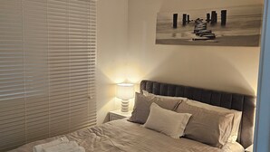 Une chambre à coucher avec un lit, un ventilateur de plafond, une fenêtre avec des stores, une lampe de chevet et un tableau au mur.