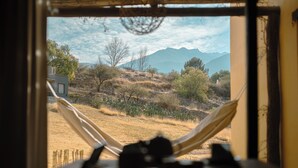 A hammock in a window overlooking a dry landscape with sparse vegetation and distant mountains. - Loma Puskana - Hostería (Cachi)