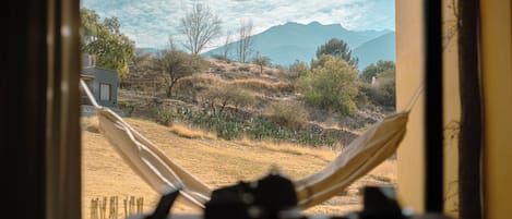 Una hamaca en una ventana con vistas a un paisaje seco y vegetación escasa, con montañas a lo lejos.