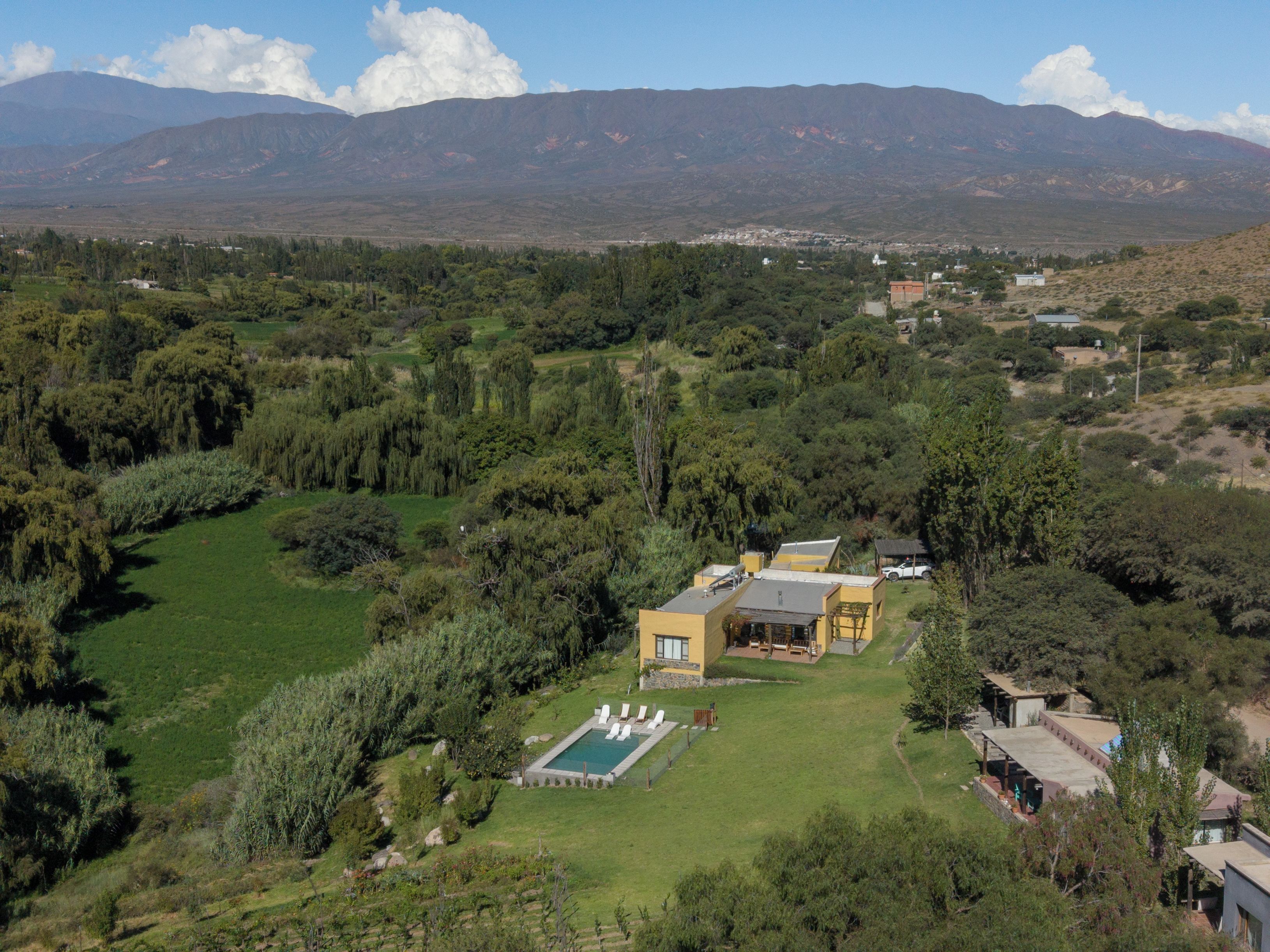 A residential area with a large house featuring a swimming pool, surrounded by lush greenery and mountains in the background.