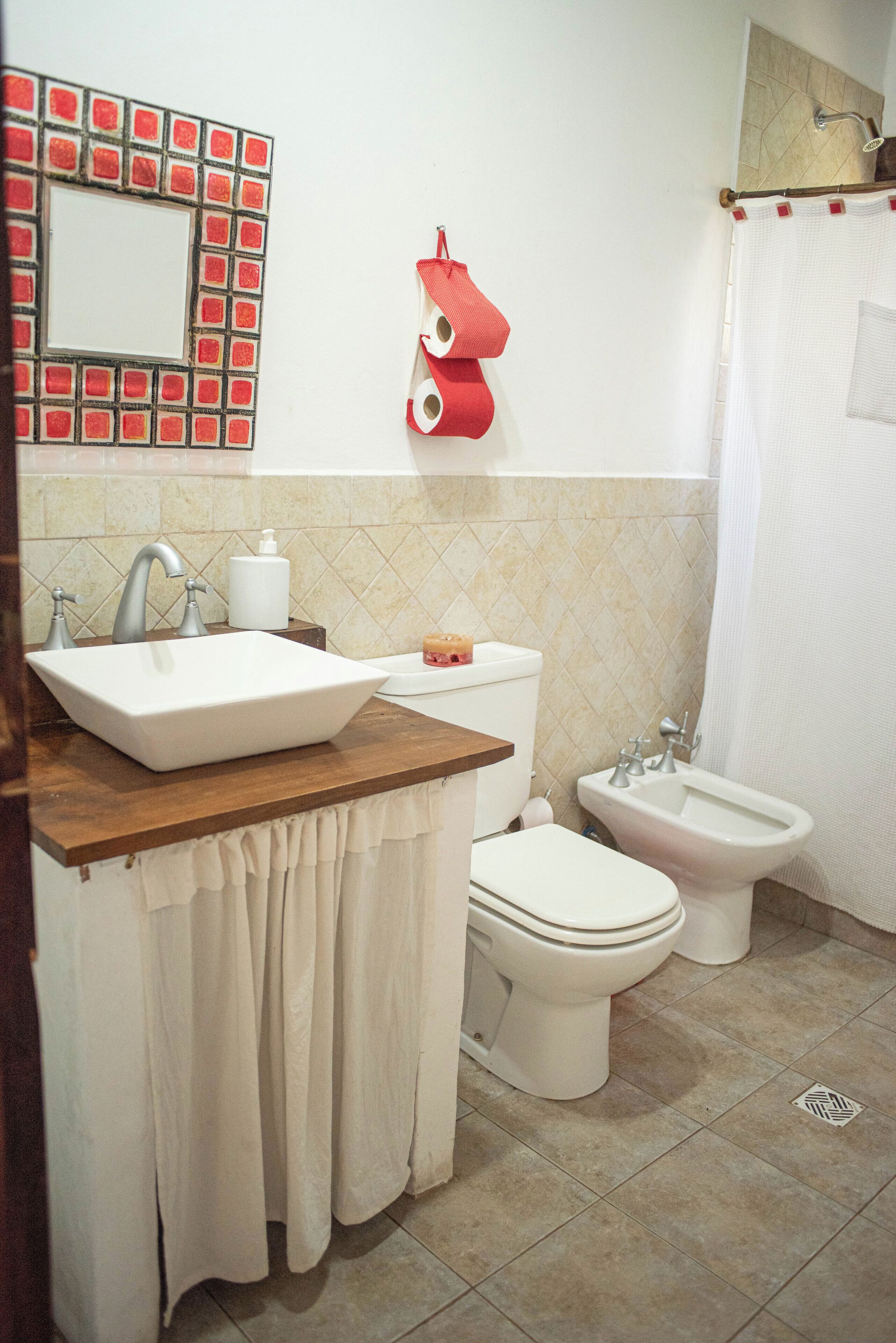 A bathroom with a sink, toilet, bidet, and a mirror with a red frame.