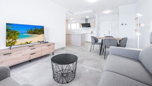 A modern living room with a flat-screen TV, grey sofa, and a round coffee table. - Principado Arena 20 Deluxe Apartment Levante Beach (Benidorm)