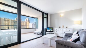 Ein modernes Wohnzimmer mit Balkon, einem Flachbildfernseher, einem grauen Sofa und einem weißen Couchtisch.