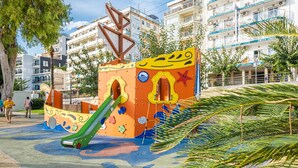 Une aire de jeux colorée, dotée d’un toboggan et d’éléments d’escalade, entourée d’immeubles et d’arbres.