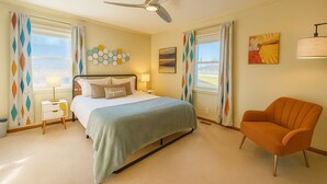 A bedroom with a bed, a nightstand, a lamp, a chair, a ceiling fan, and a window with curtains. - Unique Dwtwn+Lake & Trails (Rogers)