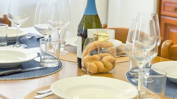 A dining table set with plates, glasses, a bottle of wine, and a basket of bread.