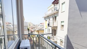 A balcony with a white air conditioning unit, metal railing, and a view of neighboring buildings.