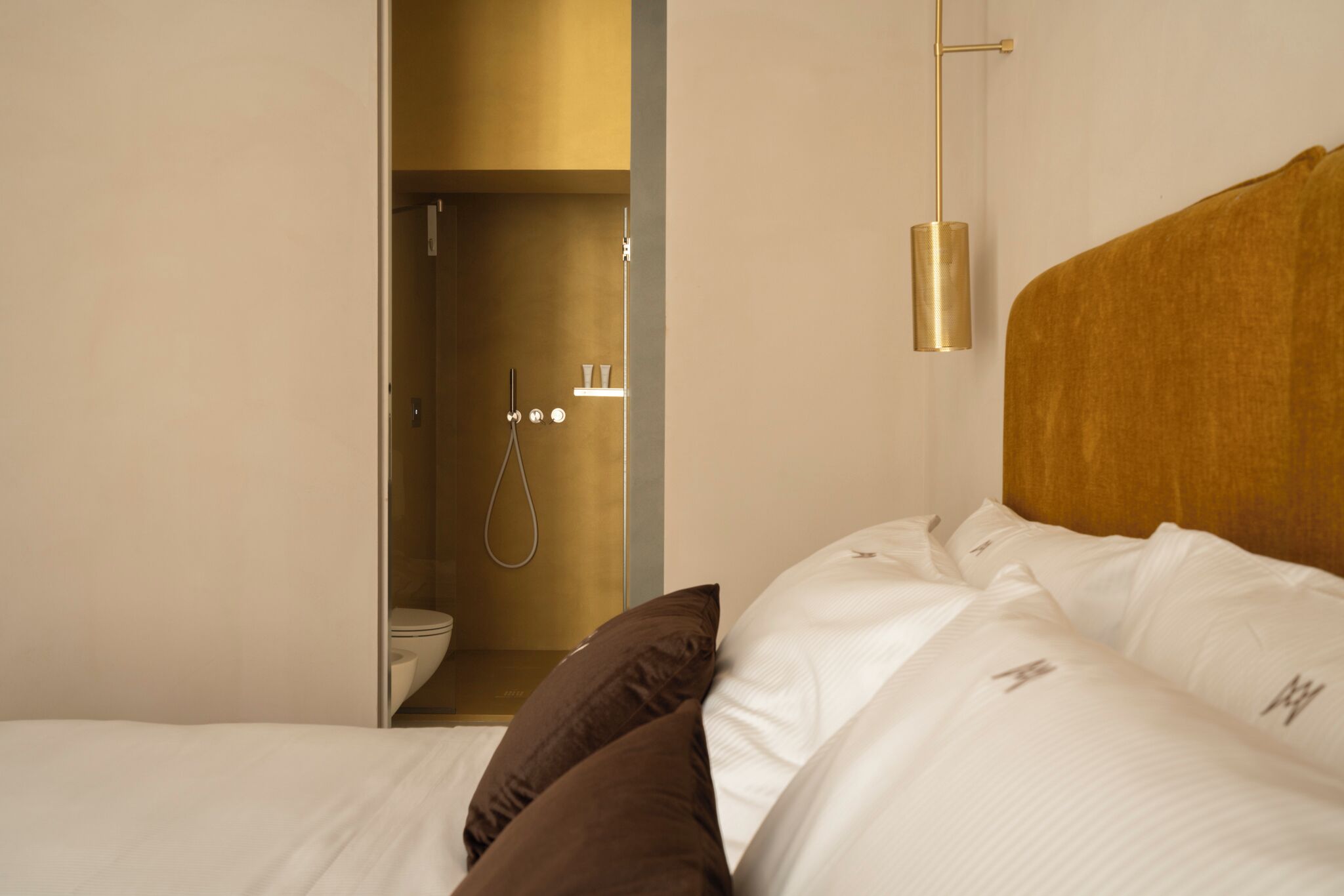 Une chambre d’hôtel avec un lit, une tête de lit en bois et un espace douche visible à travers une porte ouverte.