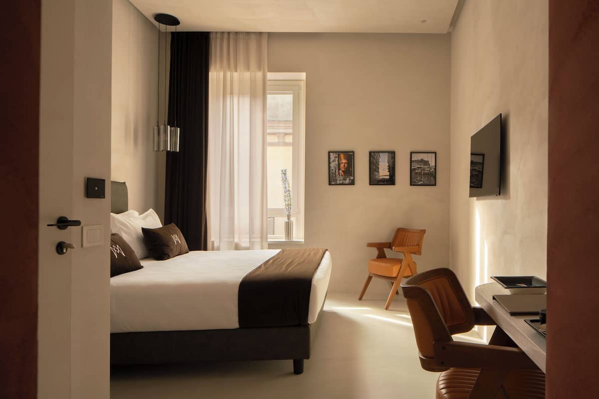 A hotel room with a bed, a desk, a chair, and a television.