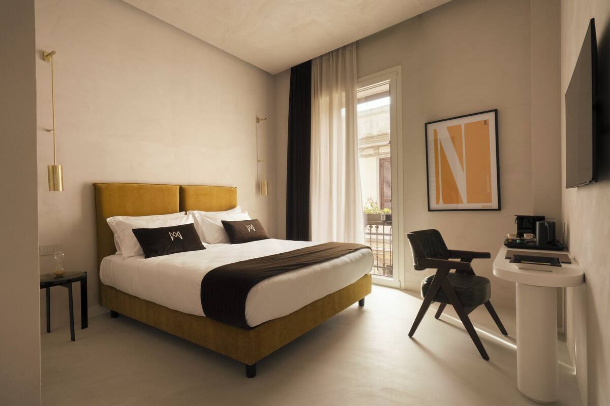 A modern hotel room with a large bed, a desk, a chair, and a TV.