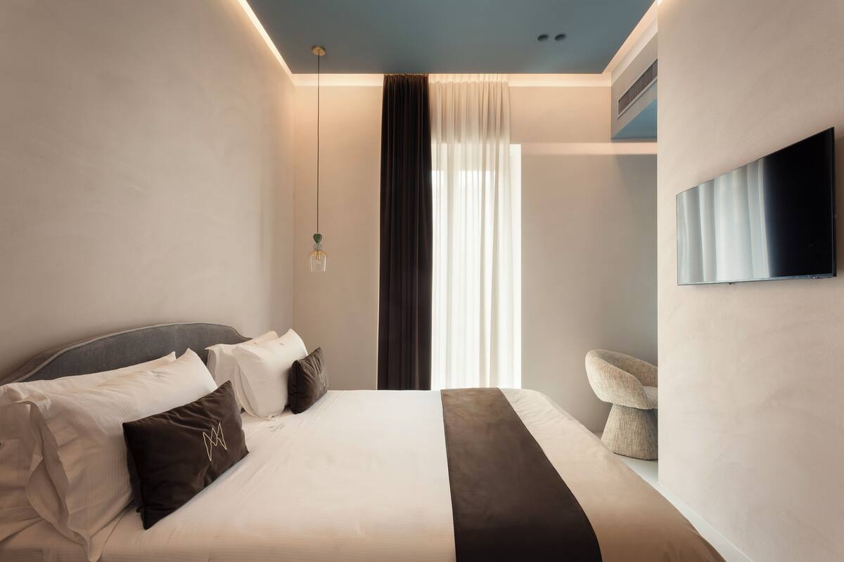 A modern hotel room with a bed, a flat-screen TV, and a seating area with a chair.