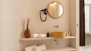 A bathroom with a round mirror, a vase with flowers, a hairdryer, a sink, and neatly folded towels. - Demetra Luxury Suites (Naples)