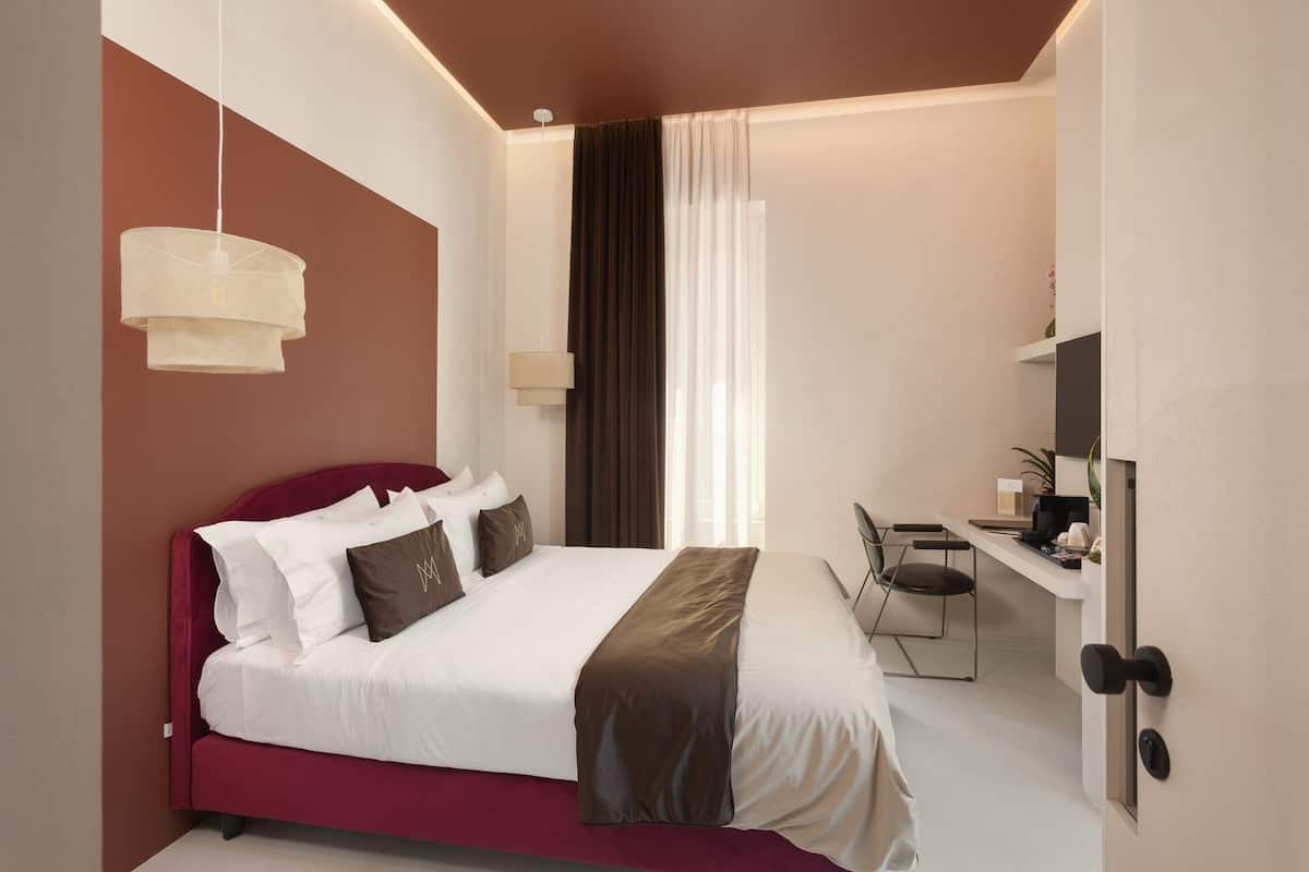 A modern hotel room with a bed, a desk, a chair, and a television.