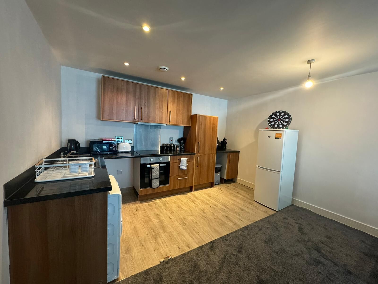 A compact kitchen with wooden cabinets, a microwave, a toaster, and a refrigerator.