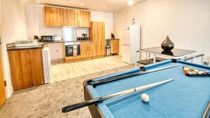 A pool table with a cue stick and balls, a kitchen area with wooden cabinets and appliances, and a dining table with a vase. - Immaculate 2-bed Apartment in Birmingham (Birmingham)