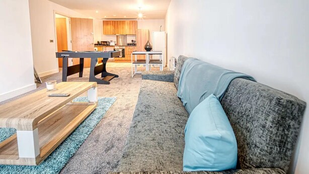 A modern living room with a grey sofa, a wooden coffee table, and a kitchen area in the background. - Immaculate 2-bed Apartment in Birmingham (Birmingham)