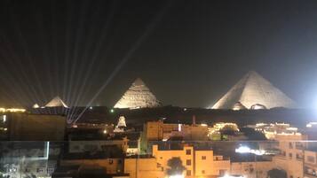 Vista nocturna de una ciudad con pirámides iluminadas al fondo y edificios en primer plano.
