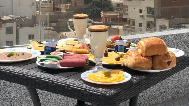 A table with food and drinks, overlooking a pyramid and a cityscape. - Middle East Pyramids View (Giza)