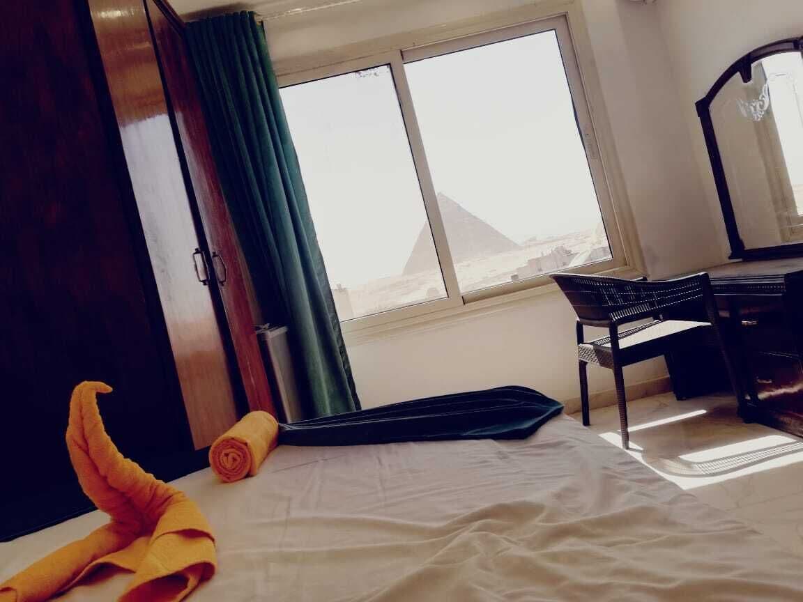 Una habitación de hotel con cama, escritorio y vista a una pirámide a través de la ventana.