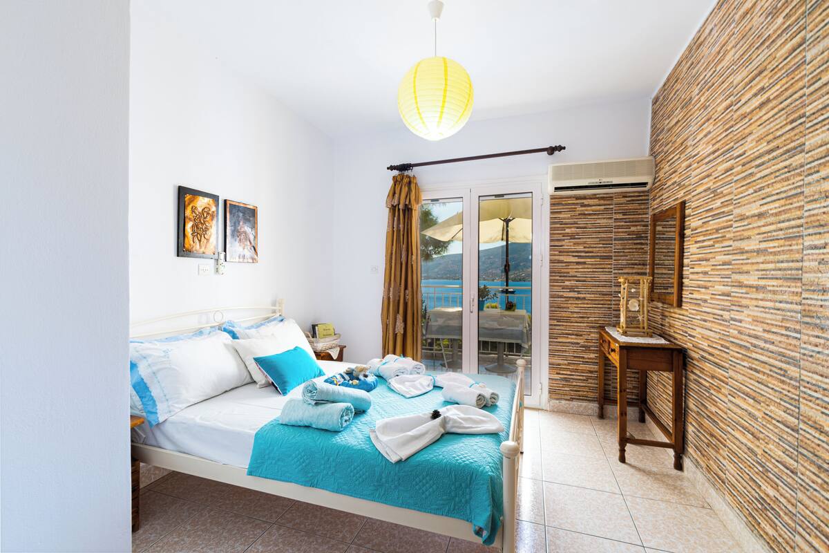 A bedroom with a bed, a bedside table, a nightstand, a window with curtains, and a view of the outdoors.